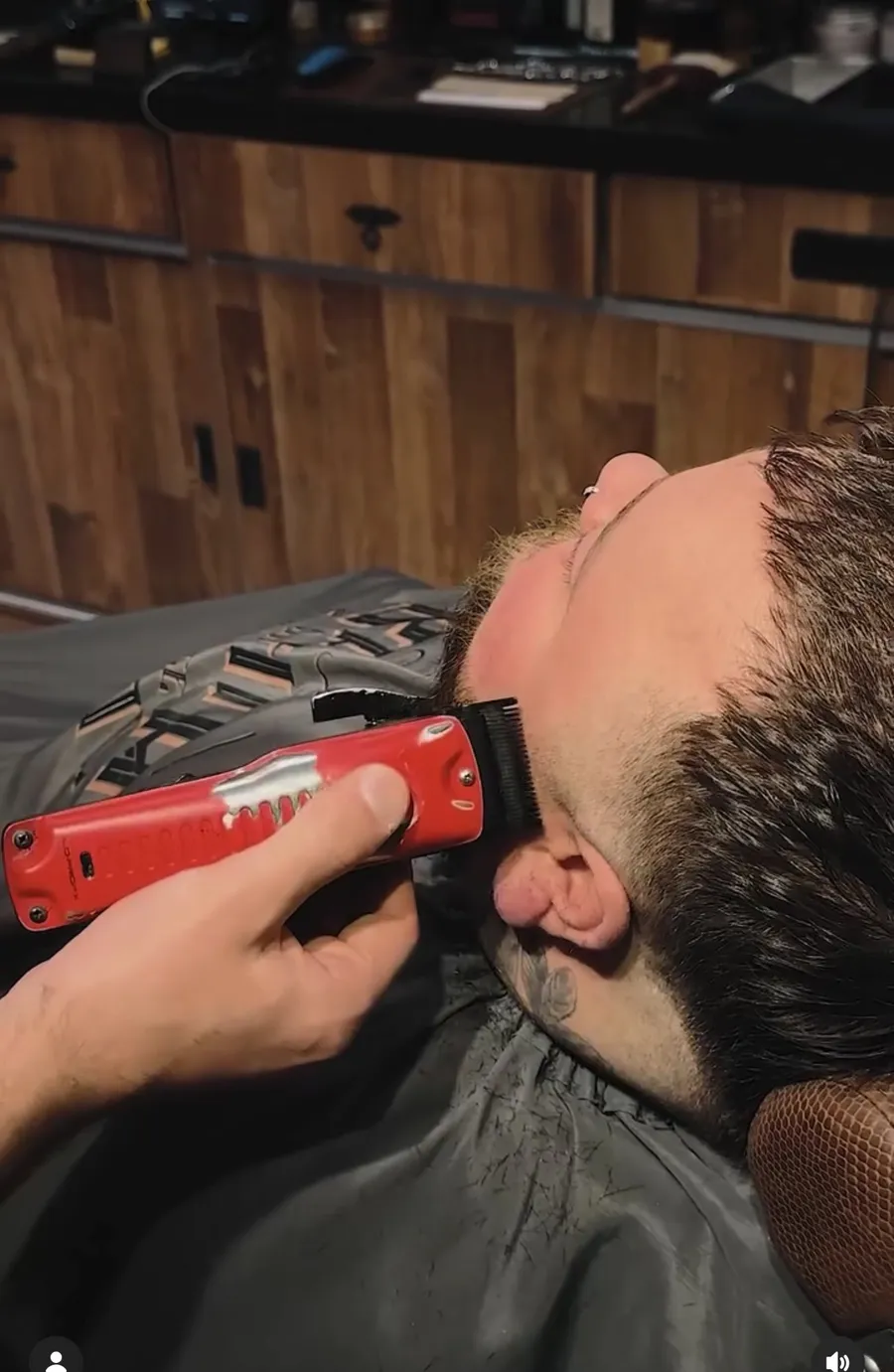 Barbeiro aparando a barba de um cliente com máquina vermelha