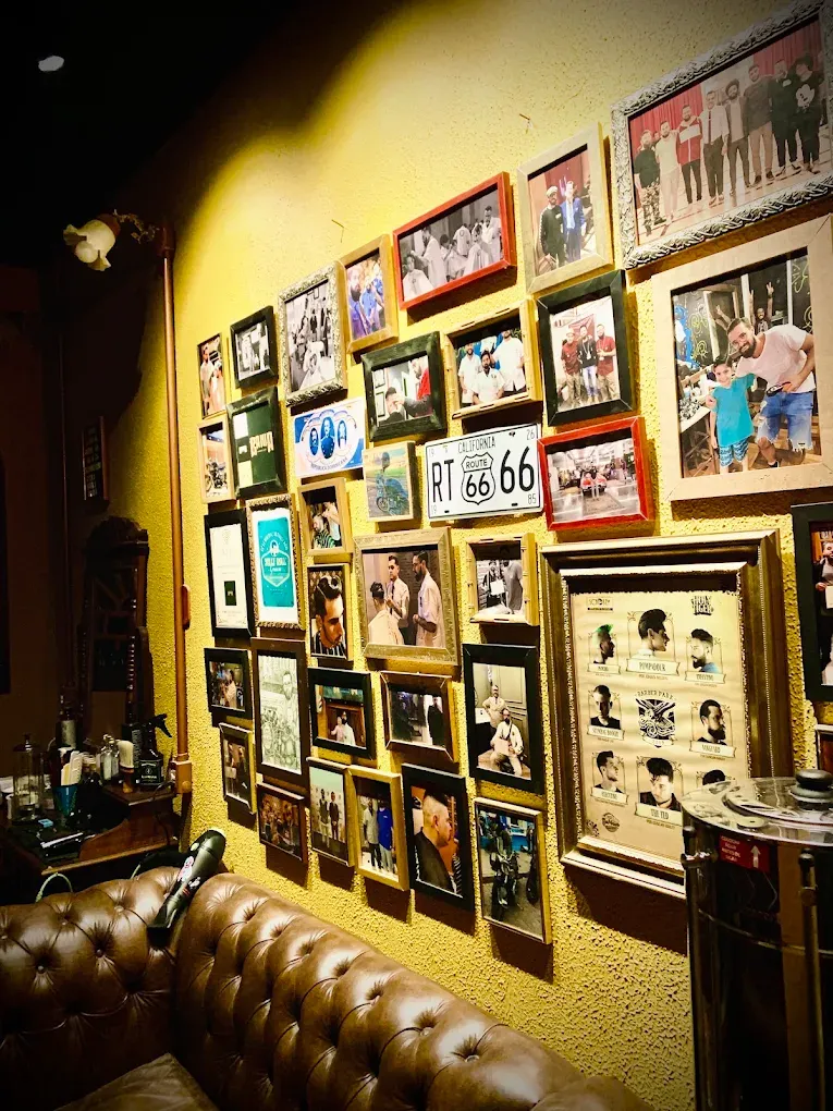 Parede amarela cheia de quadros e fotos de clientes, com placa da Route 66 e sofá Chesterfield
